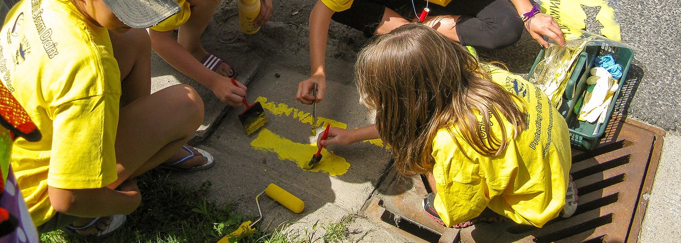 Children painting yellow fish next to a stormdrain